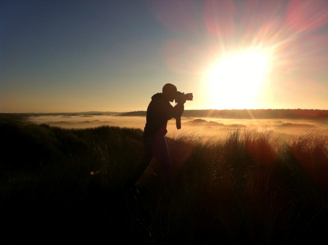 Het silhouet van een fotograaf die de mist tussen de duinen fotografeert bij zonsopkomst.